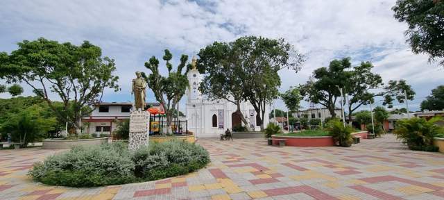 Plaza de Aracataca con una estatua, la iglesia blanca y árboles bajo un cielo nublado