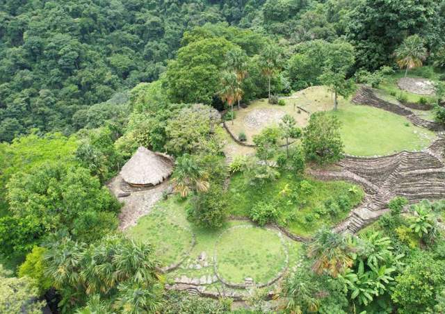 Vista aérea de terrazas de piedra y una casa ceremonial con techo de paja rodeadas de selva