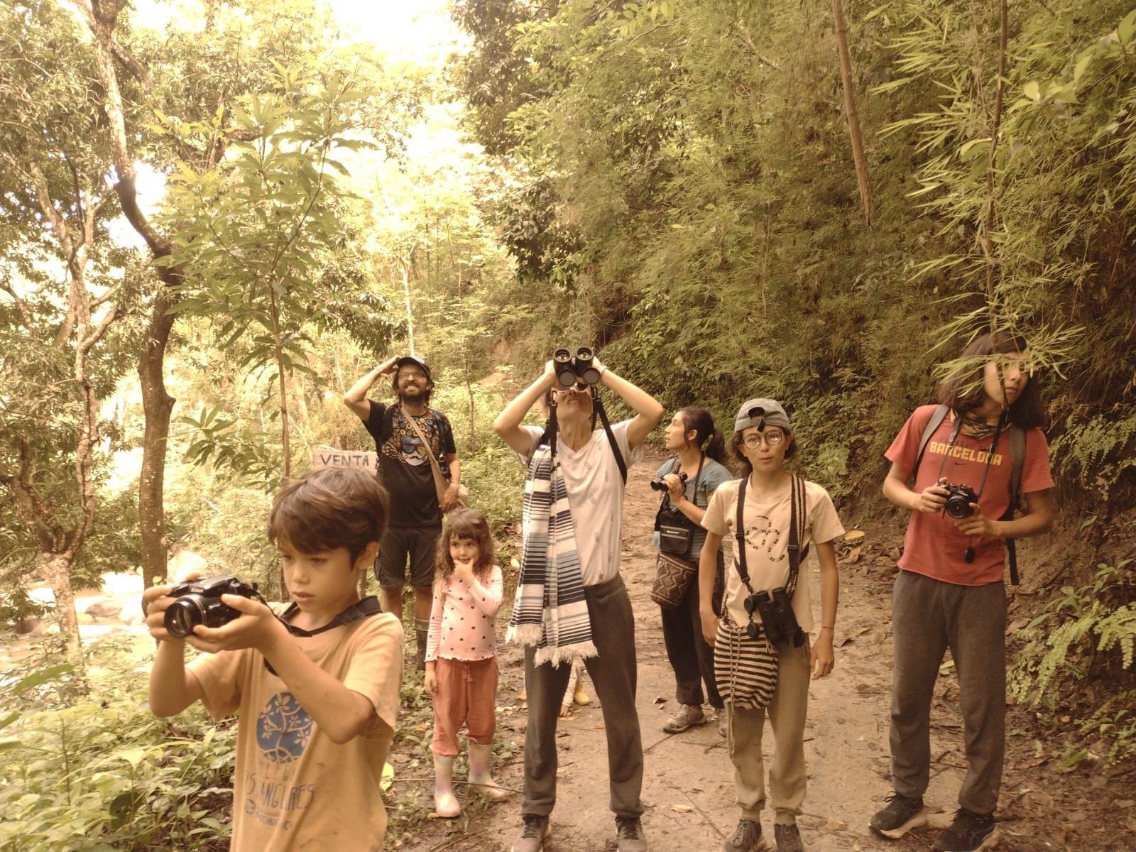Viajeros de distintas edades, entre ellos niños, observan aves con binoculares en un sendero de Luriza