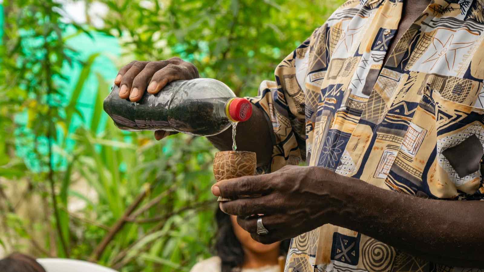 Manos que sirven una bebida tradicional desde una botella en un totumo